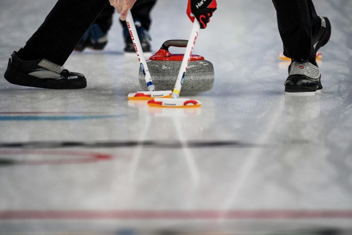 Competitors sweep in front of the curling stone during the men's bronze medal game of the Beijing 2022 Winter Olympic Games curling competition between Canada and USA at the National Aquatics Centre in Beijing on February 18, 2022.  Jeff PACHOUD / AFP
