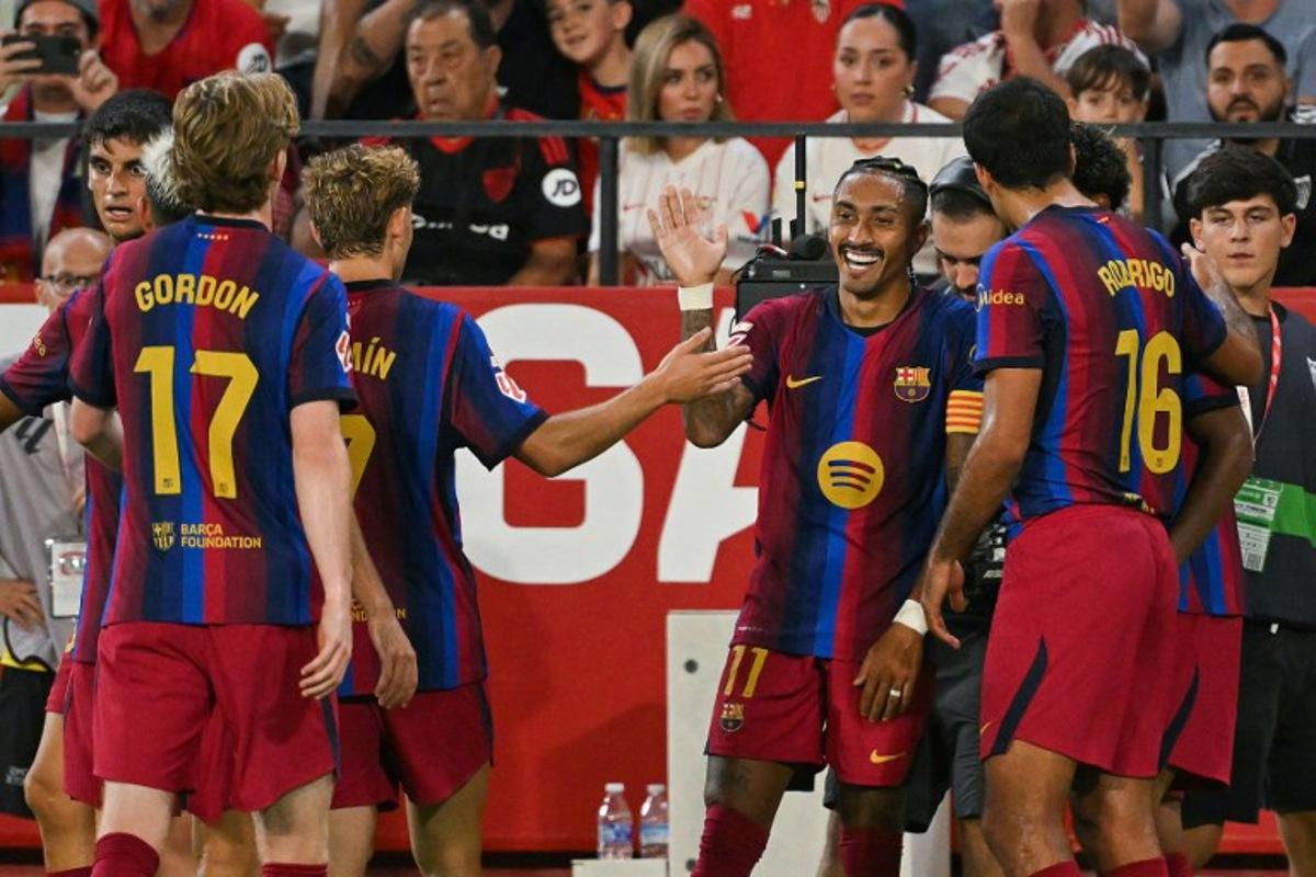 Barcelona's Brazilian forward #11 Raphinha (C) celebrates with teammates after scoring his team's third goal during the Spanish league football match between Sevilla FC and FC Barcelona at the Ramon Sanchez Pizjuan stadium in Seville on September 19, 2026.  JORGE GUERRERO / AFP