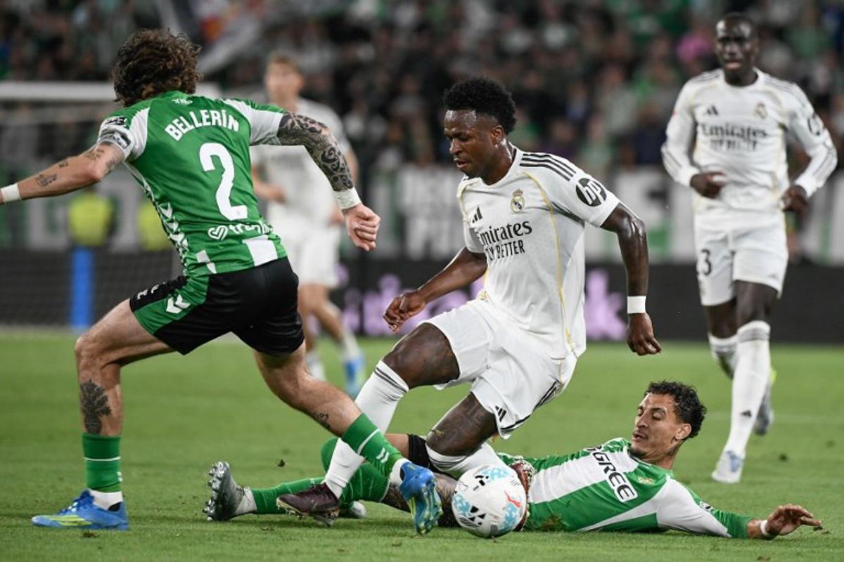 Real Madrid's Brazilian forward #07 Vinicius Junior (C) vies for the ball with Real Betis' Brazilian forward #07 Antony (R) and Real Betis' Spanish defender #02 Hector Bellerin during the Spanish league football match between Real Betis and Real Madrid CF at the La Cartuja stadium in Seville on April 24 , 2026.  CRISTINA QUICLER / AFP