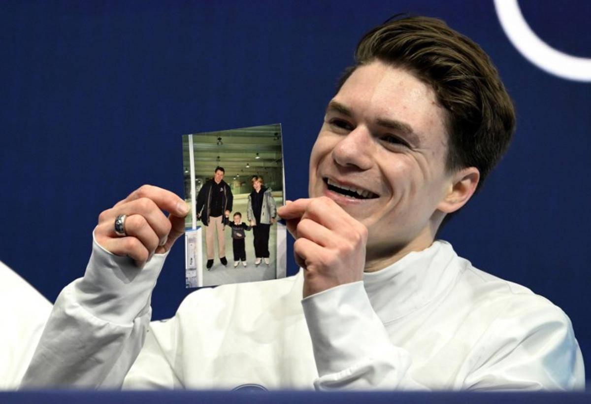 USA's Maxim Naumov holds a picture of his parents, who died in a plane crash last year, after competing in the figure skating men's singles short program during the Milano Cortina 2026 Winter Olympic Games at Milano Ice Skating Arena in Milan on February 10, 2026. Naumov's parents Vadim Naumov and Evgenia Shishkova died after a mid-air collision of an American Airlines plane and an US Army helicopter in Washington DC on January 29, 2025. WANG Zhao / AFP