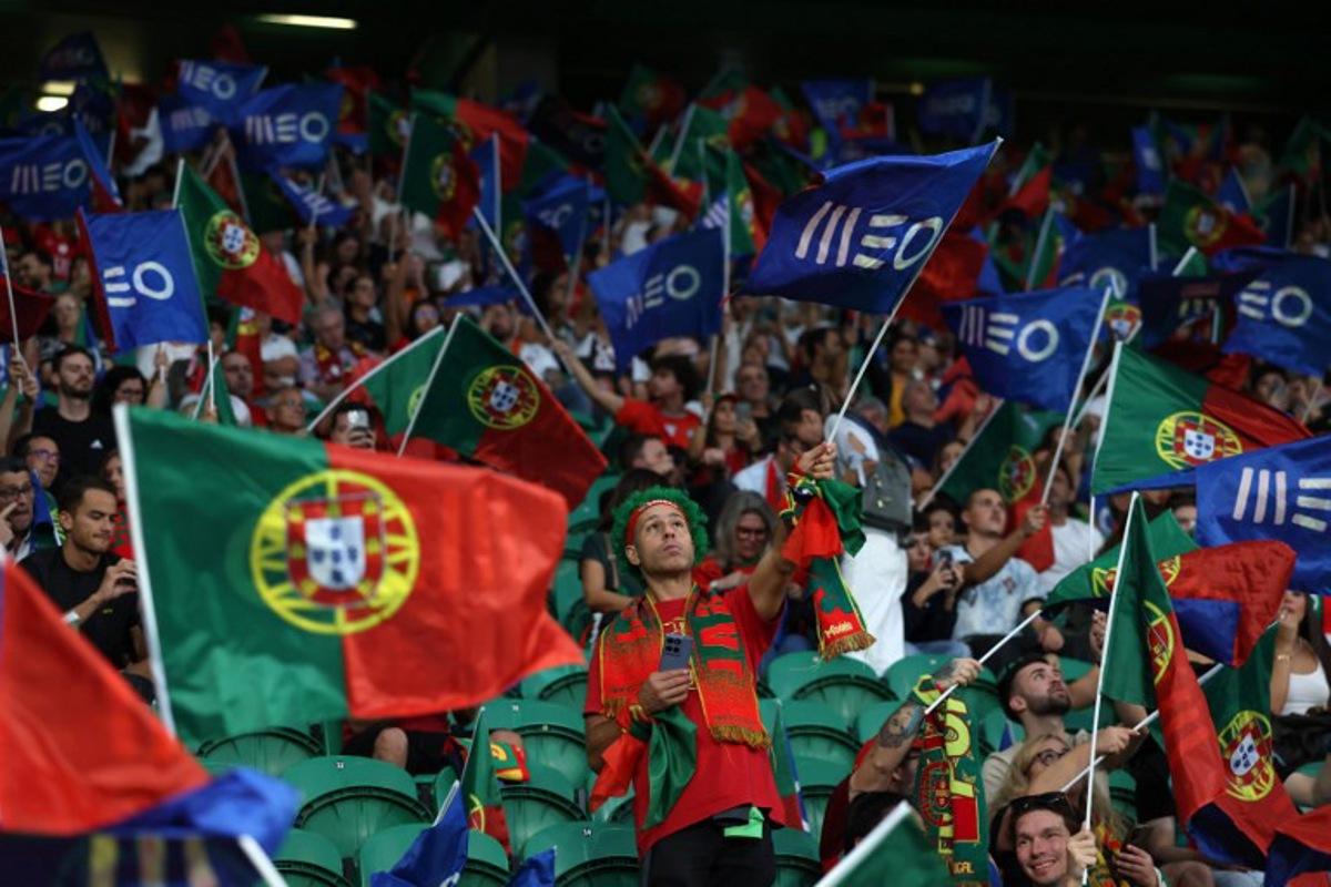 Portugal fans wave flags as they wait for the start of the 2026 World Cup qualifier Europe zone group F football match between Portugal and Ireland at Jose Alvalade stadium in Lisbon on October 11, 2025.  PATRICIA DE MELO MOREIRA / AFP