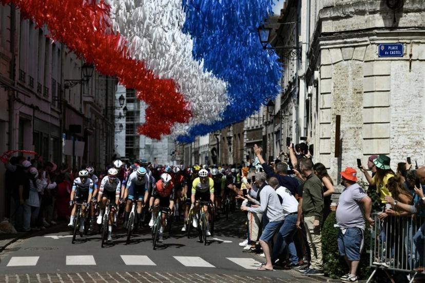 The pack of riders (peloton) cycles under decorative streamers hung above the race route in Aire-sur-la-Lys during the 3rd stage of the 112th edition of the Tour de France cycling race, 178.3 km between Valenciennes and Dunkerque (Dunkirk), Northern France, on July 7, 2025.  Marco BERTORELLO / AFP