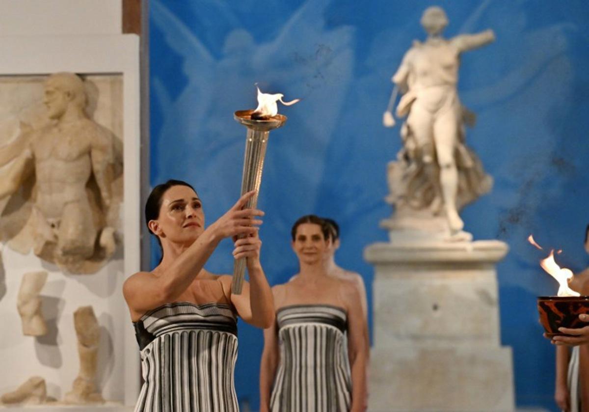 Greek actress Mary Mina (L), playing the role of the High Priestess, takes part in the flame lighting ceremony of the Olympic flame, for the Olympic Winter Games Milano Cortina 2026, at the Museum of ancient Olympia, in Olympia on November 26, 2025.  Aris MESSINIS / AFP