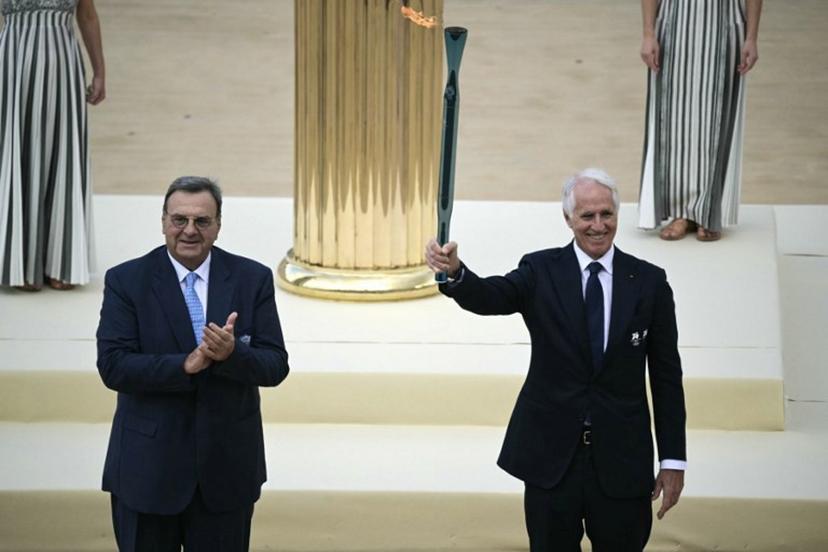 Hellenic Olympic Committee President Isidoros Kouvelos applauds as President of the Italian National Olympic Committee and CEO of the Milan Cortina 2026 Winter Olympic Giovanni Malago (R) hands the torch during the handover Olympic flame ceremony for the Milano-Cortina 2026 Winter Olympic Games and Paralympic Games, at the Panathinean stadium in Athens, on December 4, 2025.  Angelos Tzortzinis / AFP