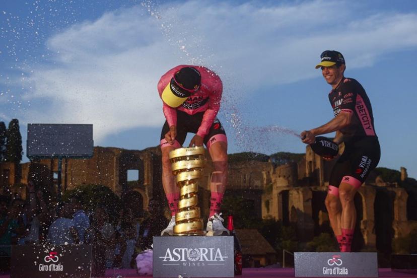 Team Visma-Lease a Bike's British rider Simon Yates (L) wearing the pink jersey of overall leader (Maglia Rosa) celebrates holding the Trofeo Senza Fine on the podium with teammate Team Visma-Lease a Bike's Belgian rider Wout Van Aert after the 21st and last stage and winning the 108th Giro d'Italia cycling race of 143kms from Rome to Rome on June 1, 2025.  Luca Bettini / AFP
