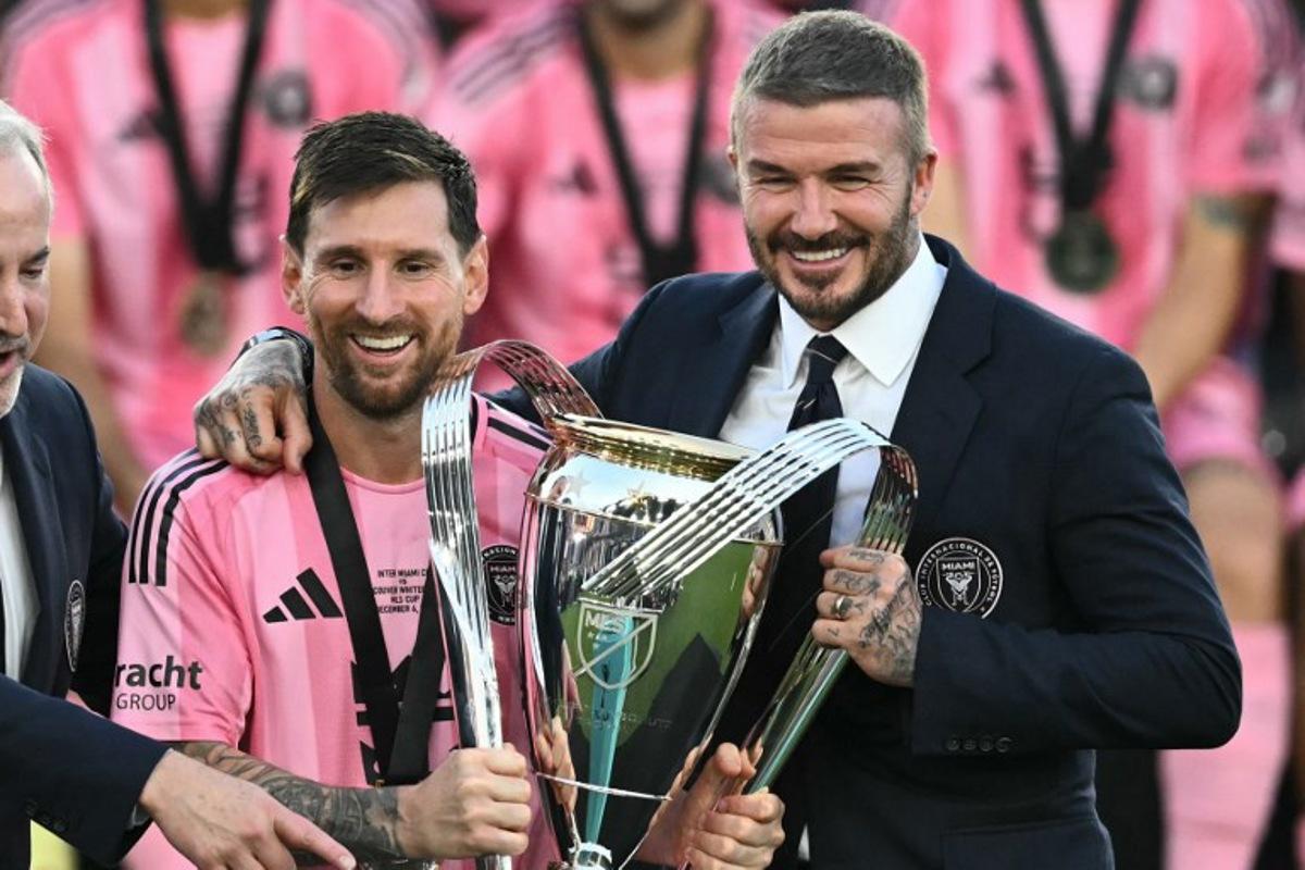 Inter Miami's Argentine forward #10 Lionel Messi (L) poses with the trophy next to the team's owner David Beckham (R) after winning the Major League Soccer (MLS) Cup final between Inter Miami and the Vancouver Whitecaps at Chase Stadium in Fort Lauderdale, Florida, on December 6, 2025. CHANDAN KHANNA / AFP