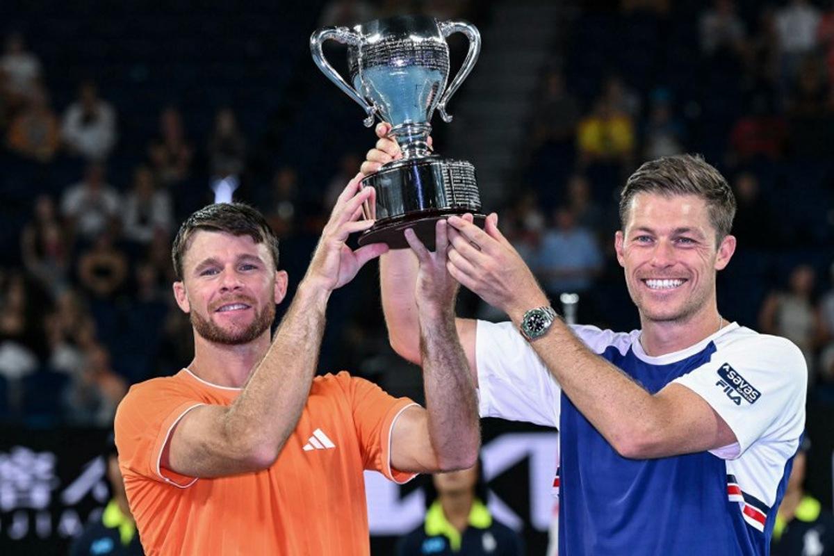 Great Britain's Neal Skupski (R) and his partner USA's Christian Harrison celebrate with the trophy after winning their men's doubles final match against Australia's Jason Kubler and Marc Polmans on day fourteen of the Australian Open tennis tournament in Melbourne on January 31, 2026. WILLIAM WEST / AFP
