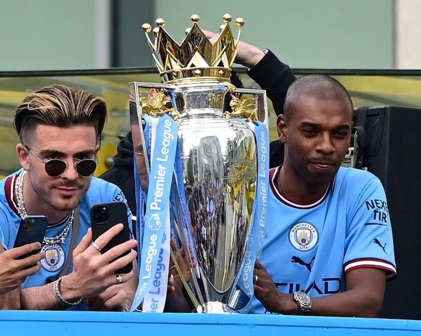 Manchester City's Brazilian midfielder Fernandinho (R) and Manchester City's English midfielder Jack Grealish (L) are seen with the trophy as Manchester City's players begin an open-top bus parade through the streets of Manchester in north-west England on May 23, 2022, to celebrate winning the 2021-22 Premier League title. Manchester City's latest Premier League title triumph established the champions as a burgeoning dynasty. City's fourth title in five seasons is arguably the greatest achievement of Guardiola's glittering career as he found a way to hold off Liverpool's relentless challenge by one point. Paul ELLIS / AFP