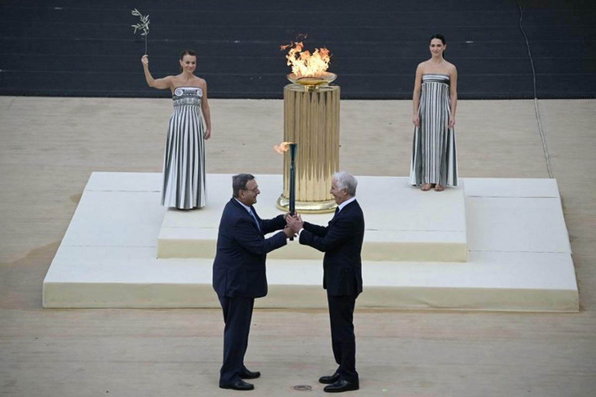 Hellenic Olympic Committee President Isidoros Kouvelos (L) and President of the Italian National Olympic Committee and CEO of the Milan Cortina 2026 Winter Olympic Giovanni Malago (R) hand the torch next to Greek actress Mary Mina playing the role of the High Priestess, during the handover Olympic flame ceremony for the Milano-Cortina 2026 Winter Olympic Games and Paralympic Games, at the Panathinean stadium in Athens, on December 4, 2025. Angelos Tzortzinis / AFP