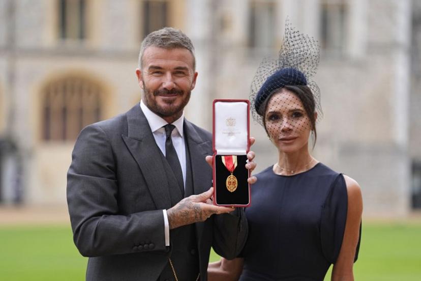 Former England footballer David Beckham (L) poses next to his wife singer and fashion designer Victoria Beckham (R) with his medal after being appointed as a Knight Bachelor (Knighthood) for services to sport and charity at an investiture ceremony at Windsor Castle on November 4, 2025.   Andrew Matthews / POOL / AFP