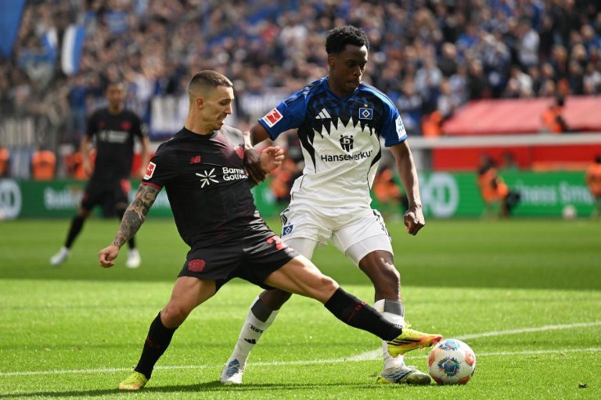Bayer Leverkusen's Spanish defender #20 Alejandro Grimaldo and Hamburg's Belgian-Congolese midfielder #06 Albert Sambi Lokonga vie for the ball during the German first division Bundesliga football match between Bayer Leverkusen and Hamburger SV (HSV) in Leverkusen, western Germany, on May 16, 2026. INA FASSBENDER / AFP
