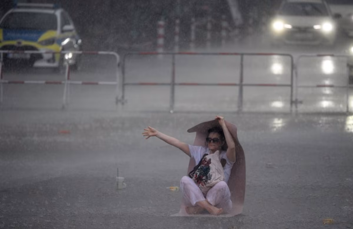 A woman uses a yoga mat to take shelter from the pouring rain as she takes part in the international yoga day, on June 21, 2026 in Berlin, Germany. RALF HIRSCHBERGER / AFP