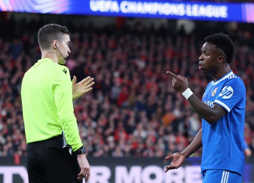 Real Madrid's Brazilian forward #07 Vinicius Junior talks with French referee Francois Letexier during the UEFA Champions League knockout round play-off first leg football match between SL Benfica and Real Madrid CF at Estadio da Luz in Lisbon on February 17, 2026. PATRICIA DE MELO MOREIRA / AFP