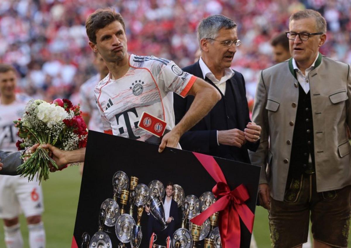 Bayern Munich's German forward #25 Thomas Mueller (L) walks away with a flower bouquet and a picture showing Muller inmid trophies ahead the German first division Bundesliga football match between Bayern Munich and Borussia Moenchengladbach in Munich on May 10, 2025. Alexandra BEIER / AFP